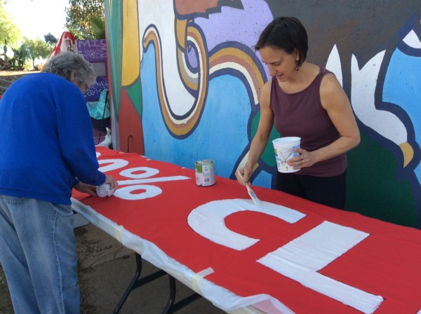 Jean Costa and Jane Blount paint "100% clean energy" onto long red banner.