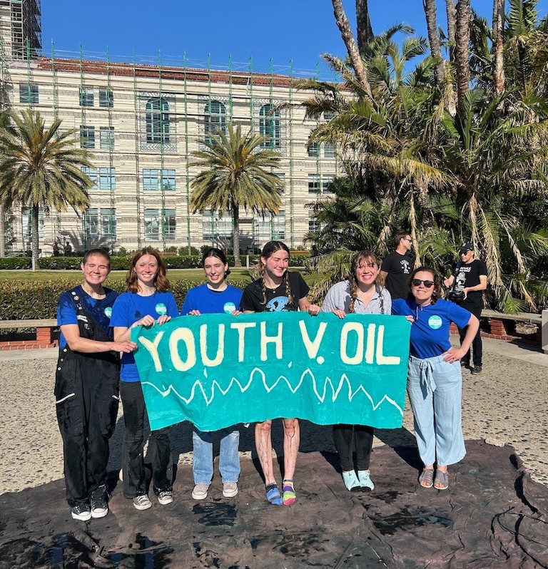 Megan Phelps and a small group of youth smiling and holding up a Youth v. Oil sign 