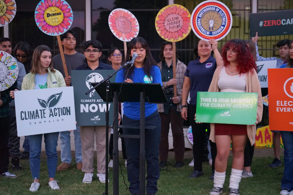 Abigail Costello, Junior at Hilltop High School and SanDiego350 intern, speaking in front of the podium and in front of youth holding signs.