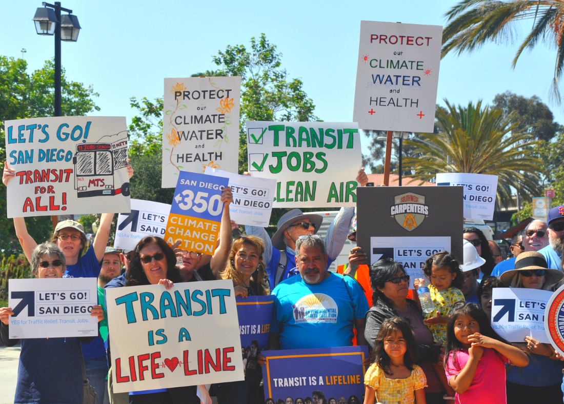 People smiling holding signs about transit