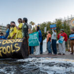 Youth members holding signs and youth members covered in oil in front of an oil barrel that reads "fossil fuels"