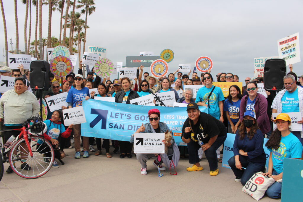 Community members and advocates holding signs behind a big Let's Go! San Diego sign