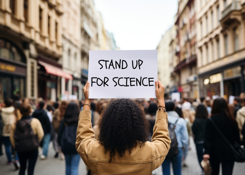 Person holding up a protest sign that reads "Stand Up for Science" 