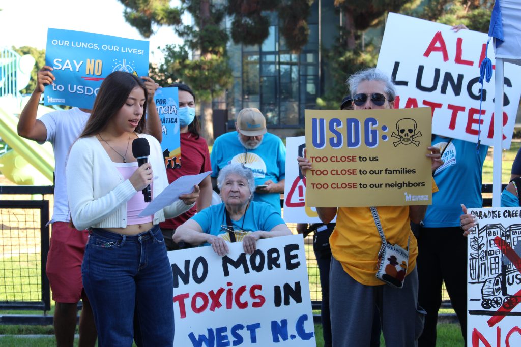 Youth member speaking in front of people holding signs