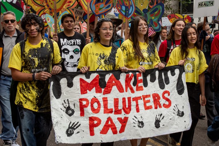 Youth holding a sign that reads "Make Polluters Pay"
