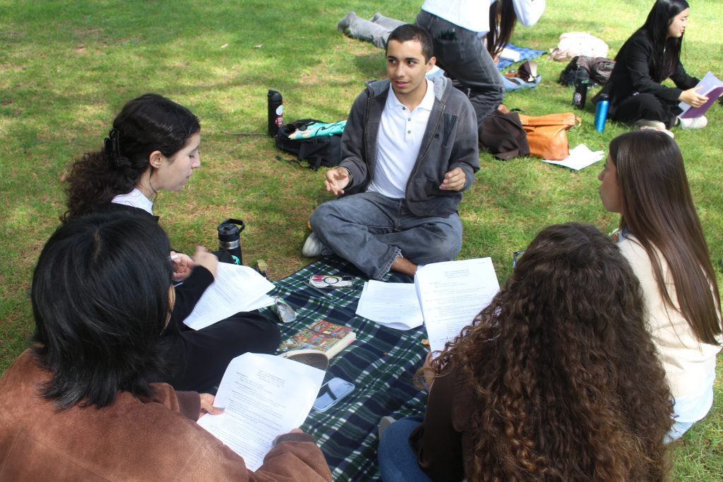 A group of youth sitting on the grass talking and reading a paper