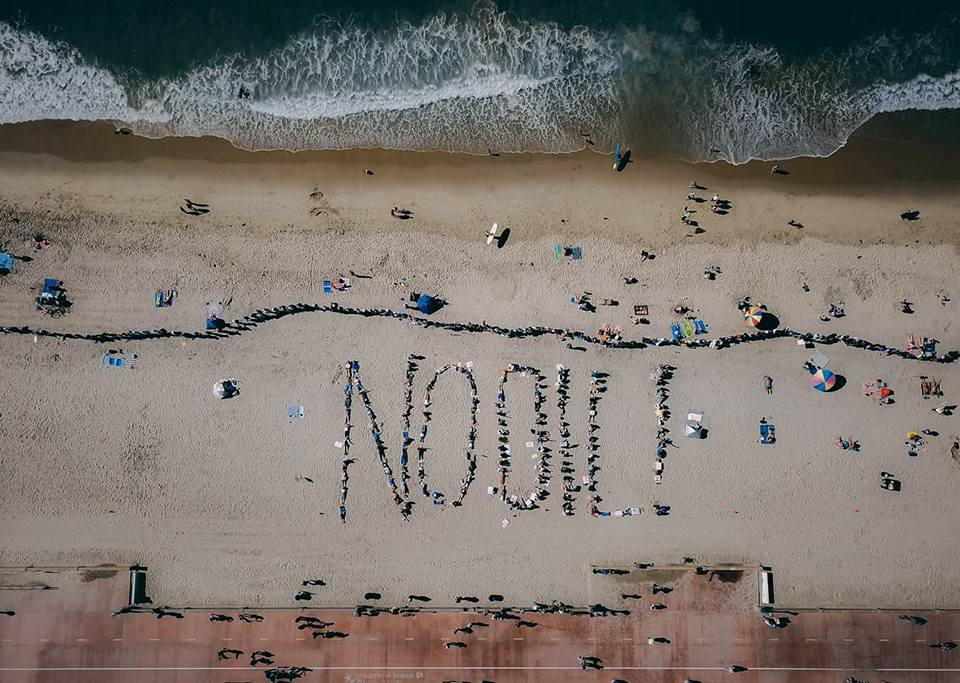 People on the beach spelling out the words "No Oil" with their bodies